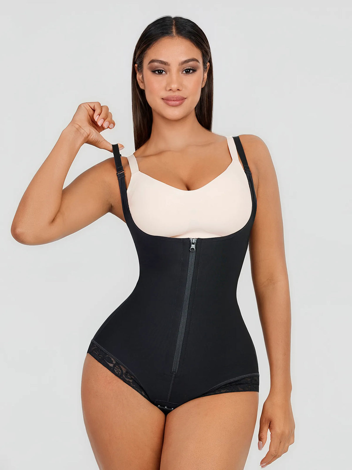 A woman modeling a black shapewear bodysuit with a front zipper and a contrasting cream underwire bra, set against a solid light gray background.