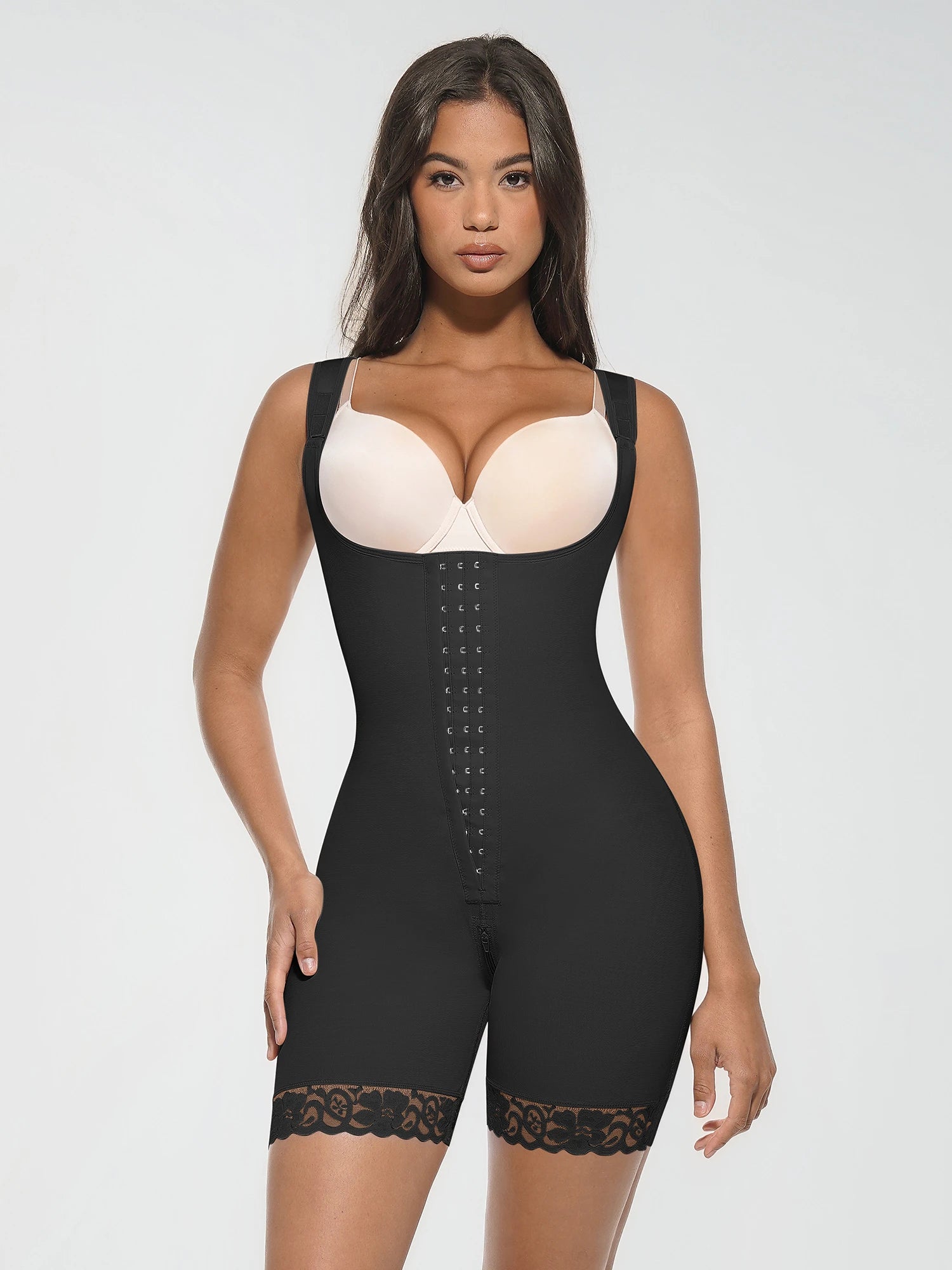Front view of a model wearing a black open-bust full body shapewear bodysuit with front hook-and-eye closure and lace-trimmed legs