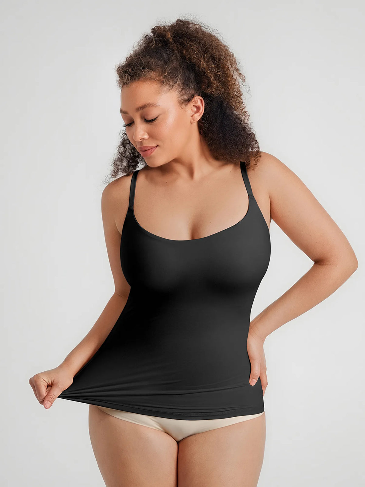 Front profile of a model stretching a black seamless scoop-neck camisole featuring dual-layer light waist smoothing mesh